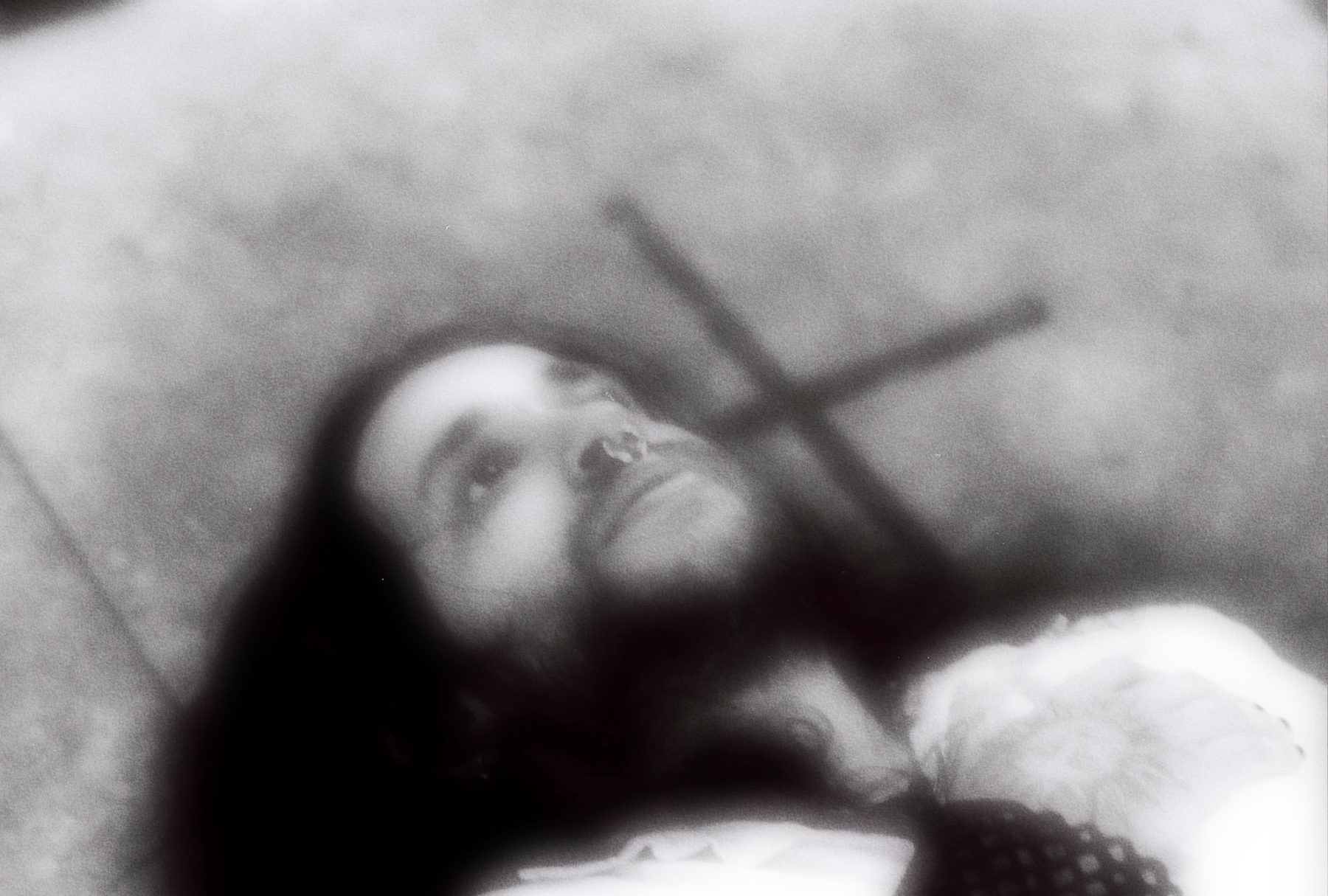 Black and white photo of durl lying beneath a stone grave cross